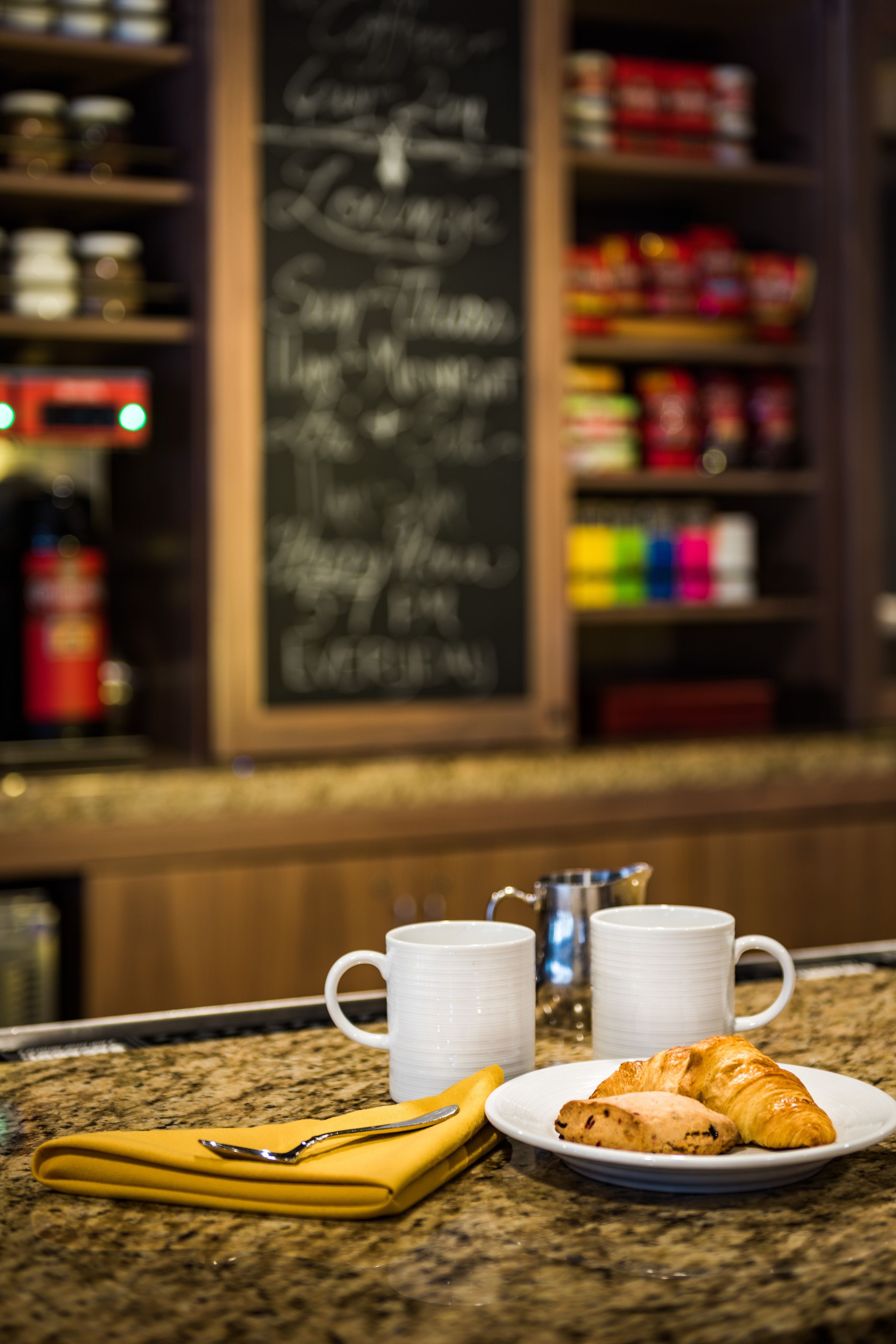 A breakfast setting with a croissant and two white mugs on a granite countertop.