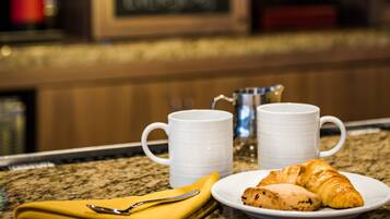 A breakfast setting with a croissant and two white mugs on a granite countertop.
