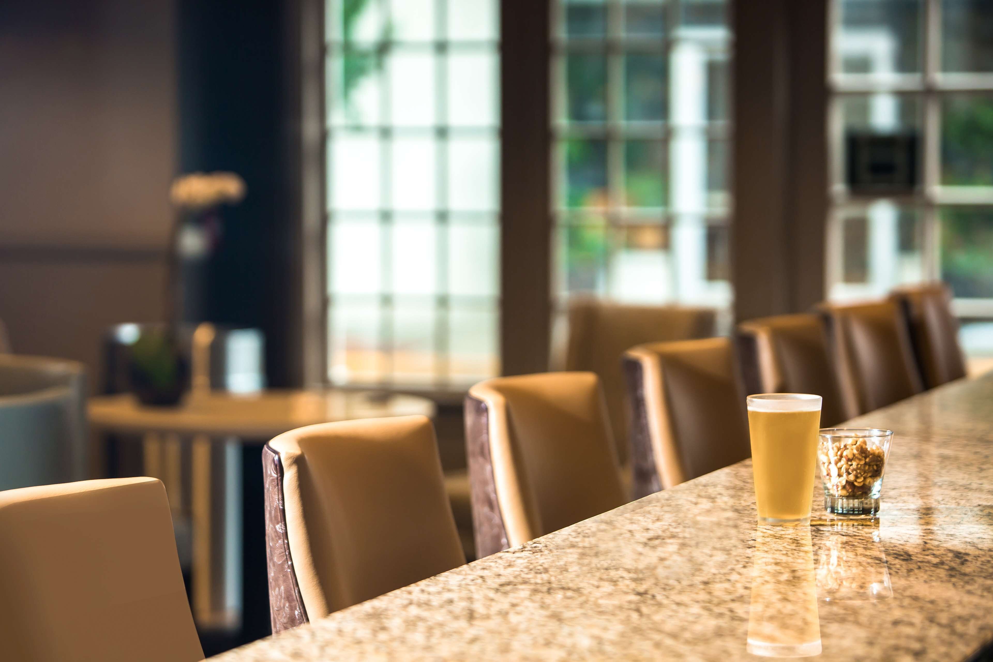A bar area with a long counter, several leather chairs, and a glass of beer.