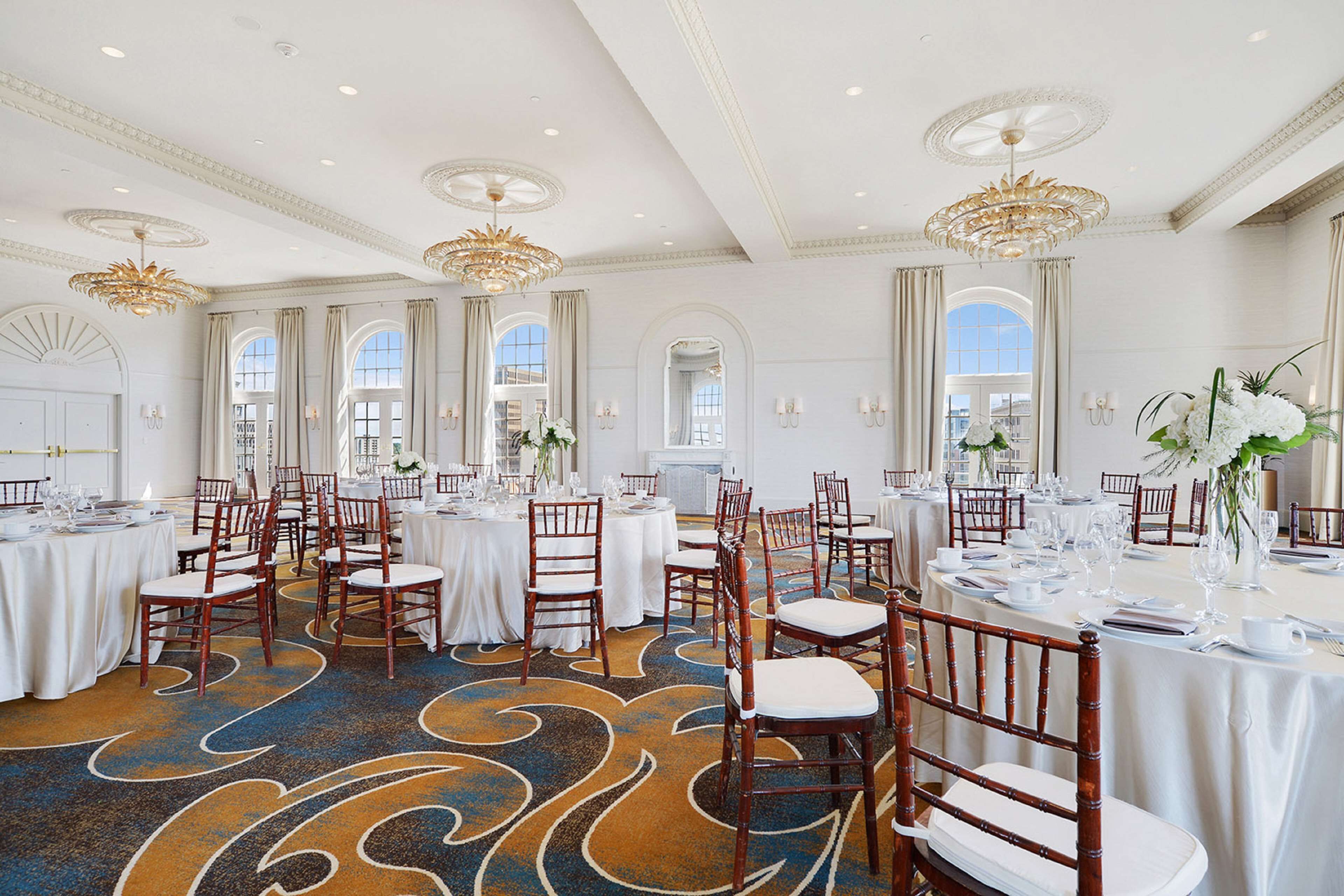Un salón de banquetes espacioso con varias mesas redondas, elegantes candelabros y una alfombra estampada.