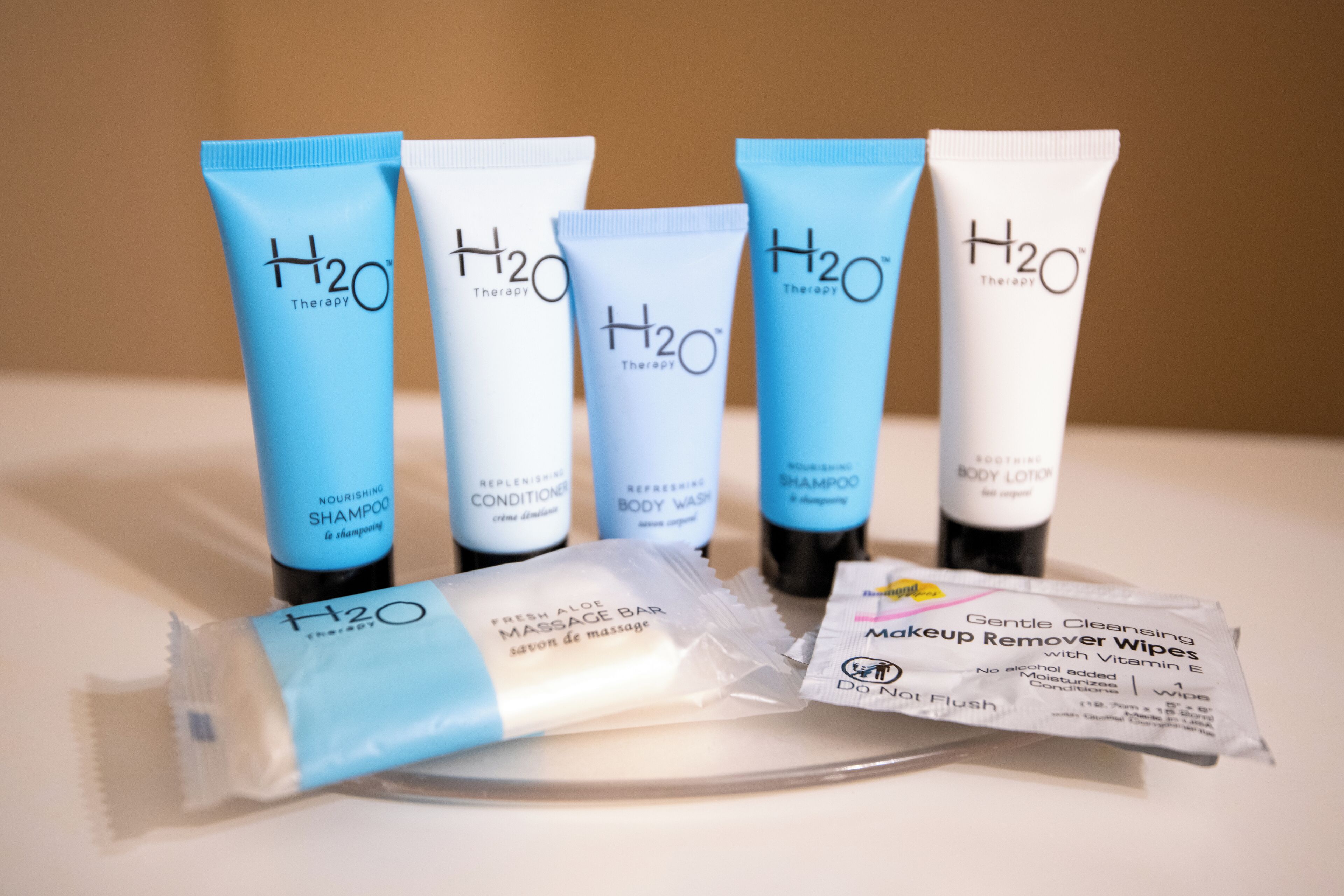 Five H2O Therapy products, including shampoo, conditioner, body wash, shampoo, and body lotion, along with a massage bar and makeup remover wipes.