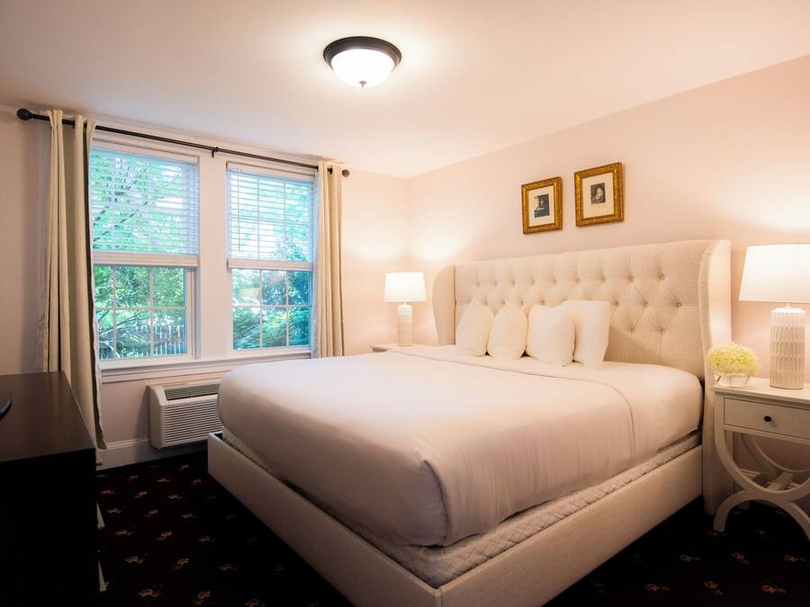 A hotel room with a large bed, two bedside lamps, a TV, and a window with curtains.