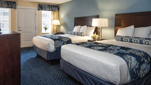 A hotel room with two beds, a desk, and a window with curtains.