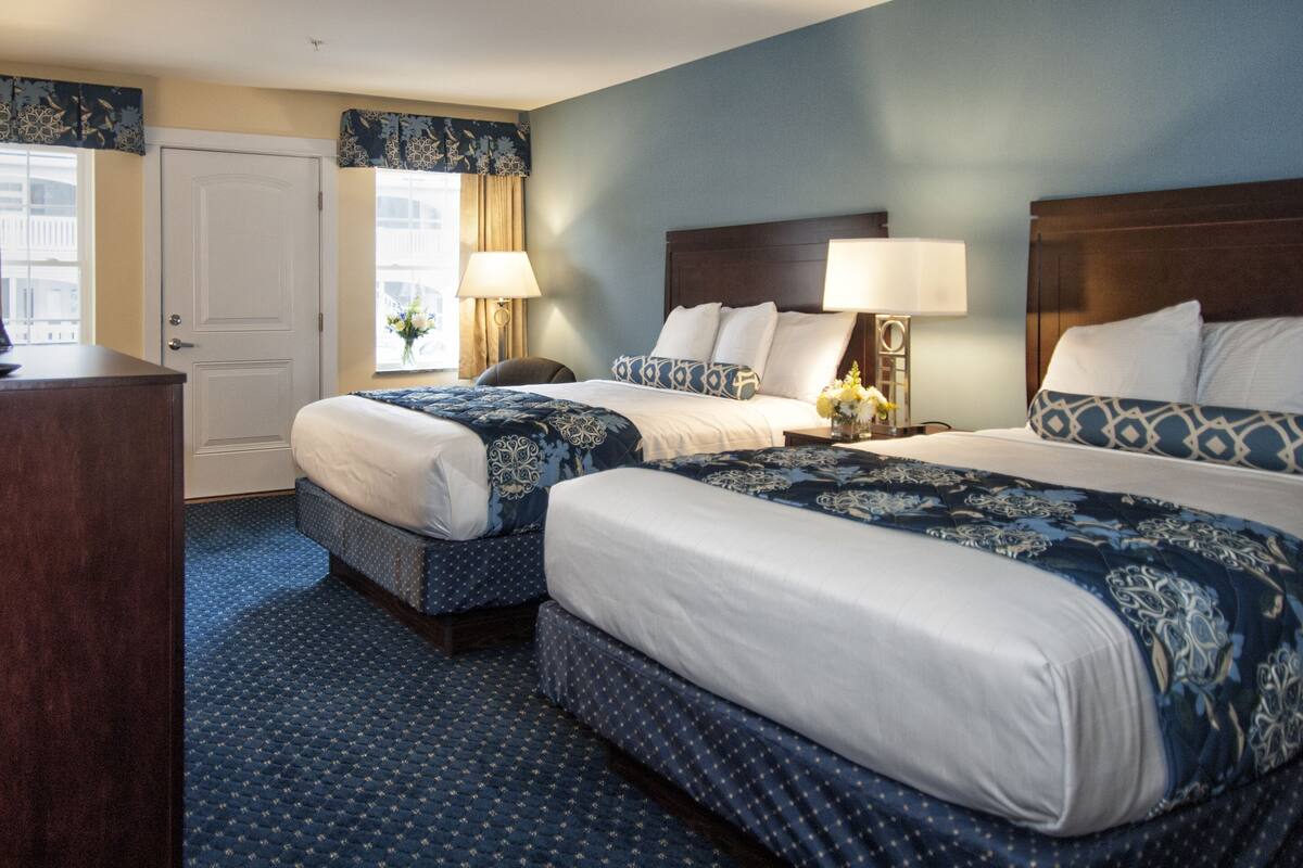 A hotel room with two beds, a desk, and a window with curtains.