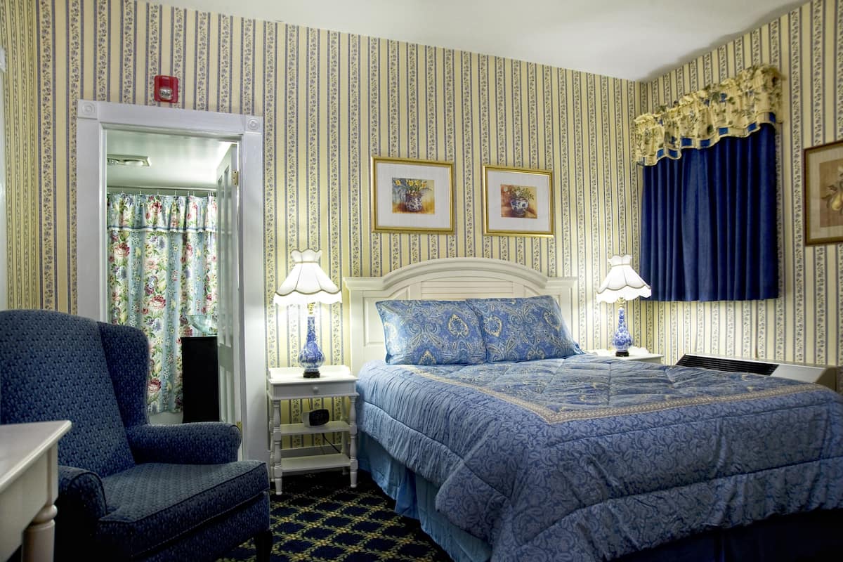 A bedroom with a bed, two bedside lamps, a nightstand, a chair, and a door leading to a bathroom.