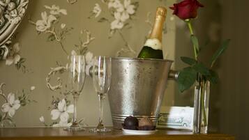 A champagne bottle in a metal bucket, two empty wine glasses, and a red rose in a vase on a table with a floral wallpaper background.