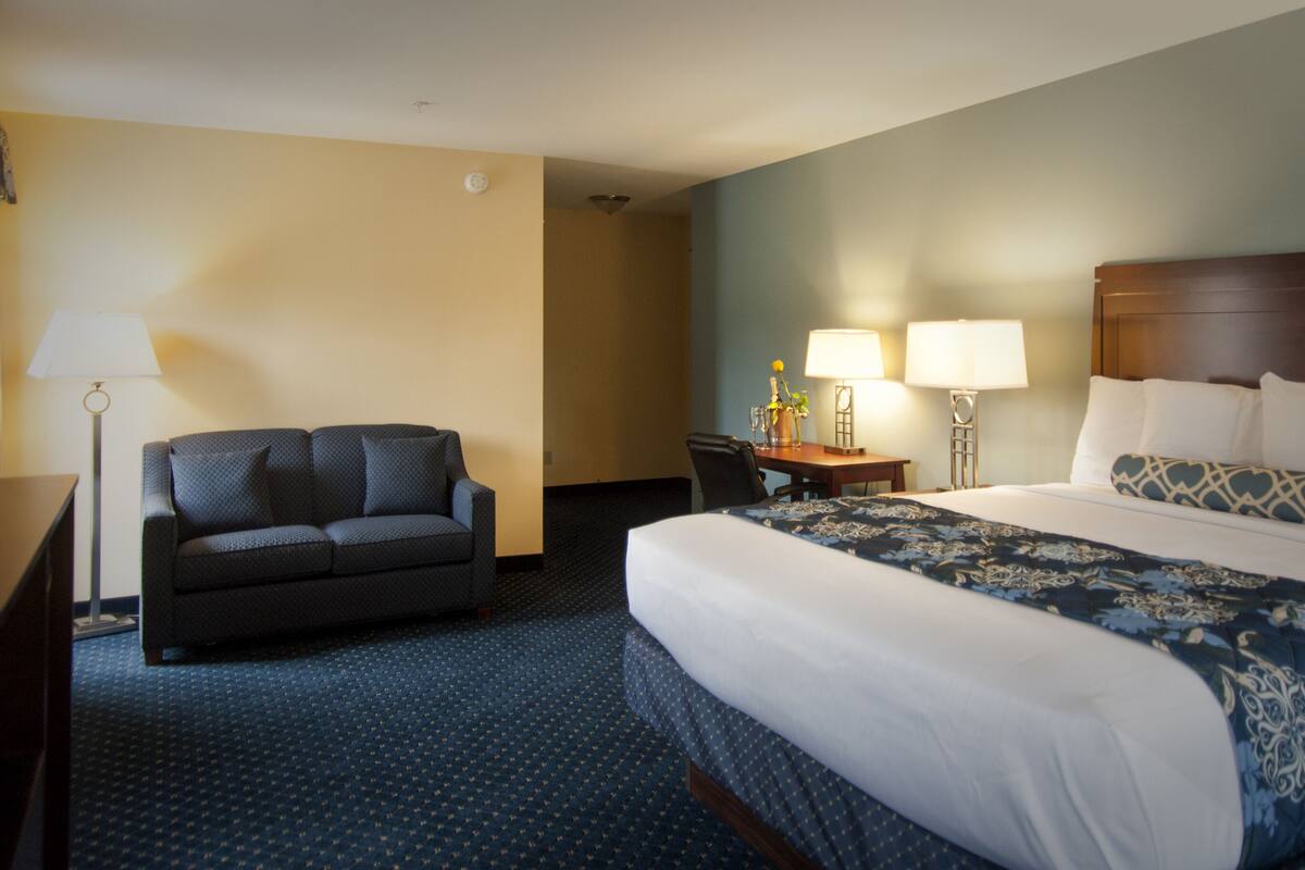 A hotel room with a large bed, a sofa, a desk, and a lamp.