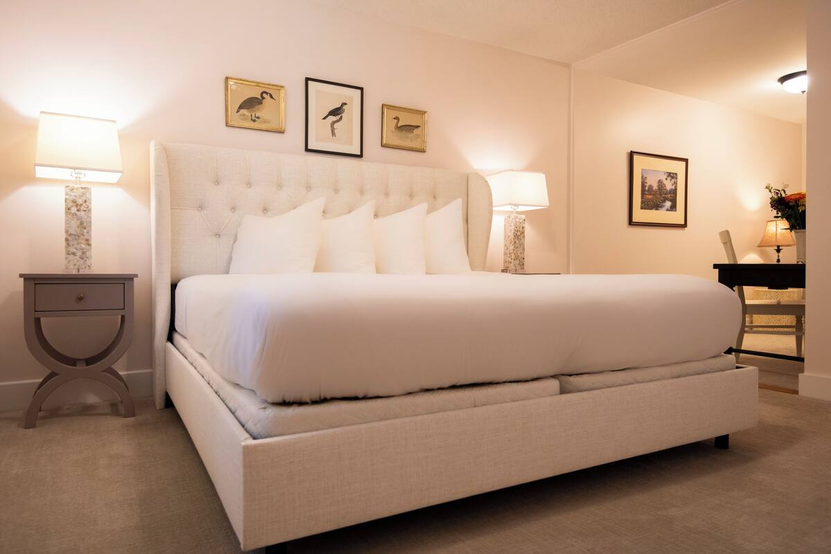 A large bed with a tufted headboard, two bedside tables with lamps, and three framed pictures on the wall.