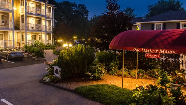 A multi-story hotel with a covered outdoor seating area, a parking lot, and a landscaped garden.