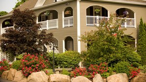 A two-story house with a porch, multiple windows, and a well-maintained garden with large rocks and flowering plants.