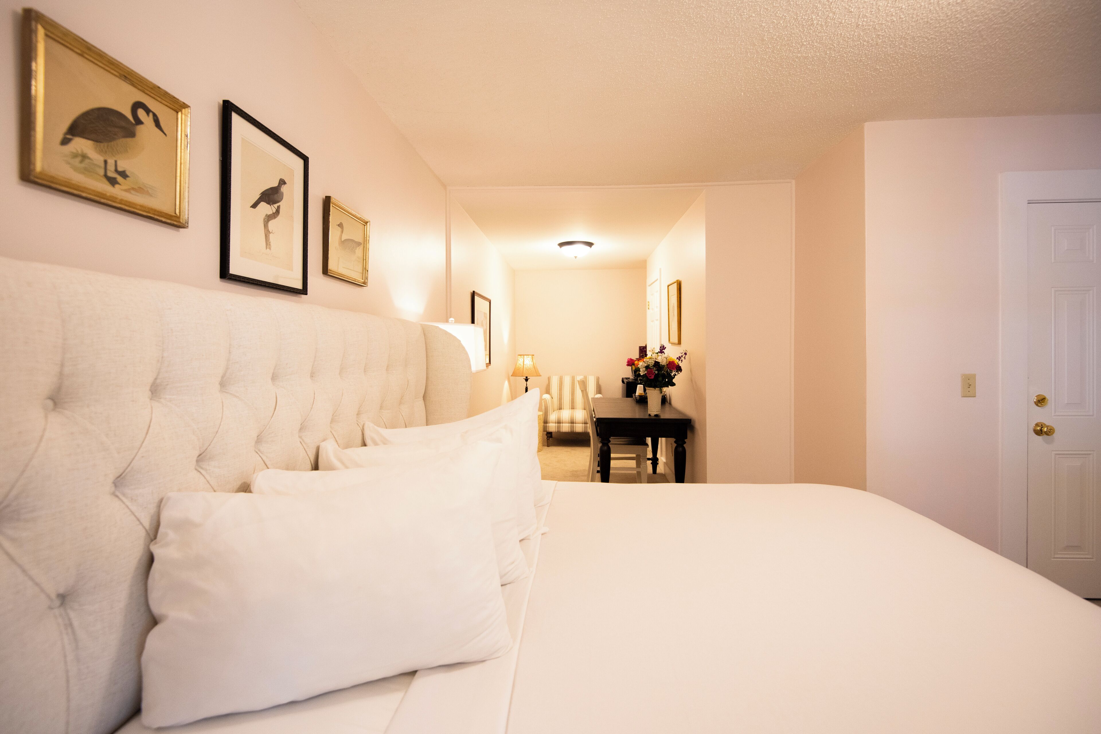 A hotel room with a large bed, a desk, and framed artwork on the wall.