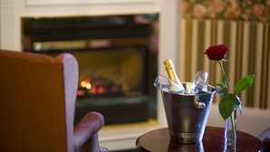 A room with a fireplace, a metal bucket with champagne glasses, and a rose in a vase.