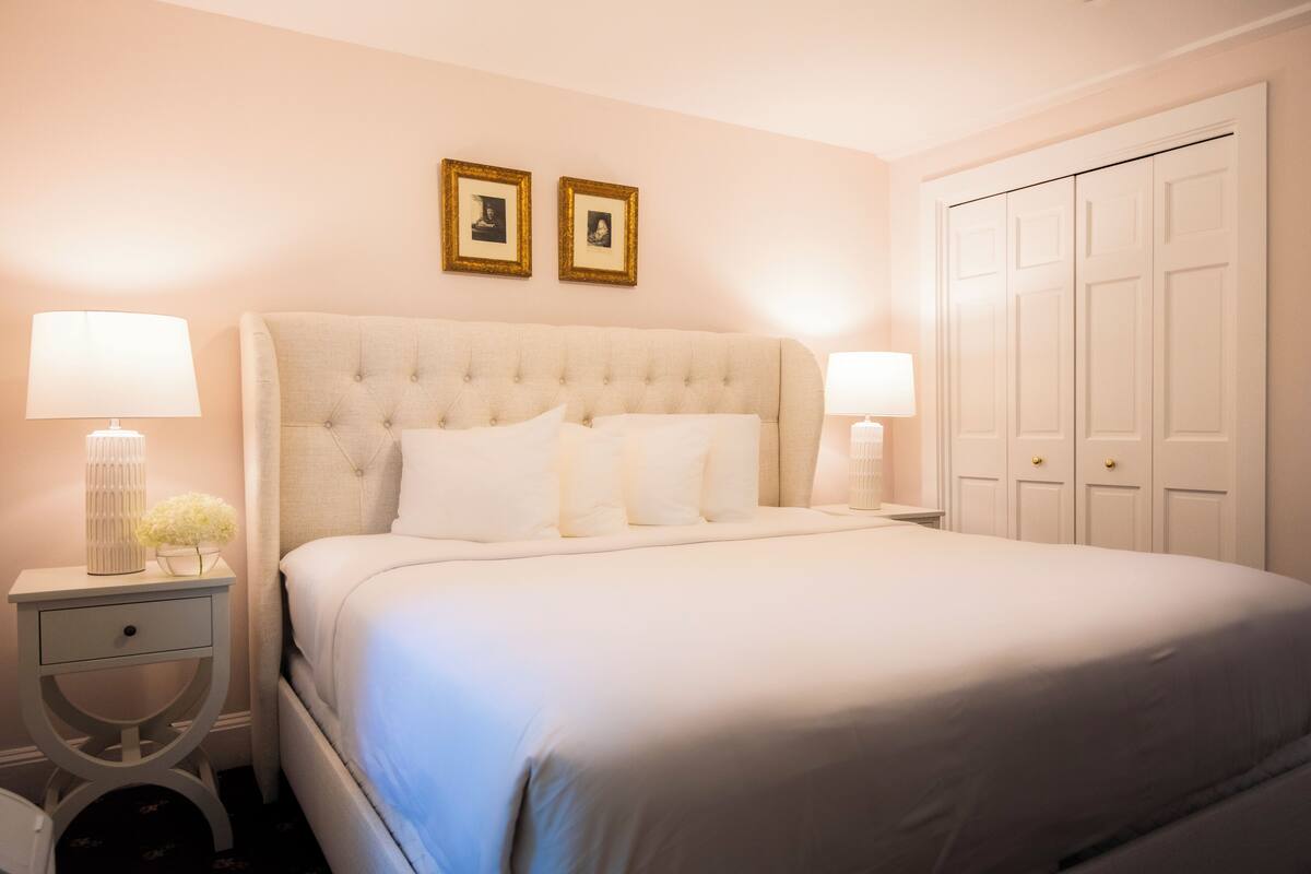 A neatly made bed with a tufted headboard, two bedside tables with lamps, and a wardrobe with multiple doors.