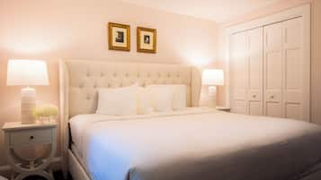 Una cama bien tendida con un cabecero capitonado, dos mesitas de noche con lámparas y un armario con varias puertas.