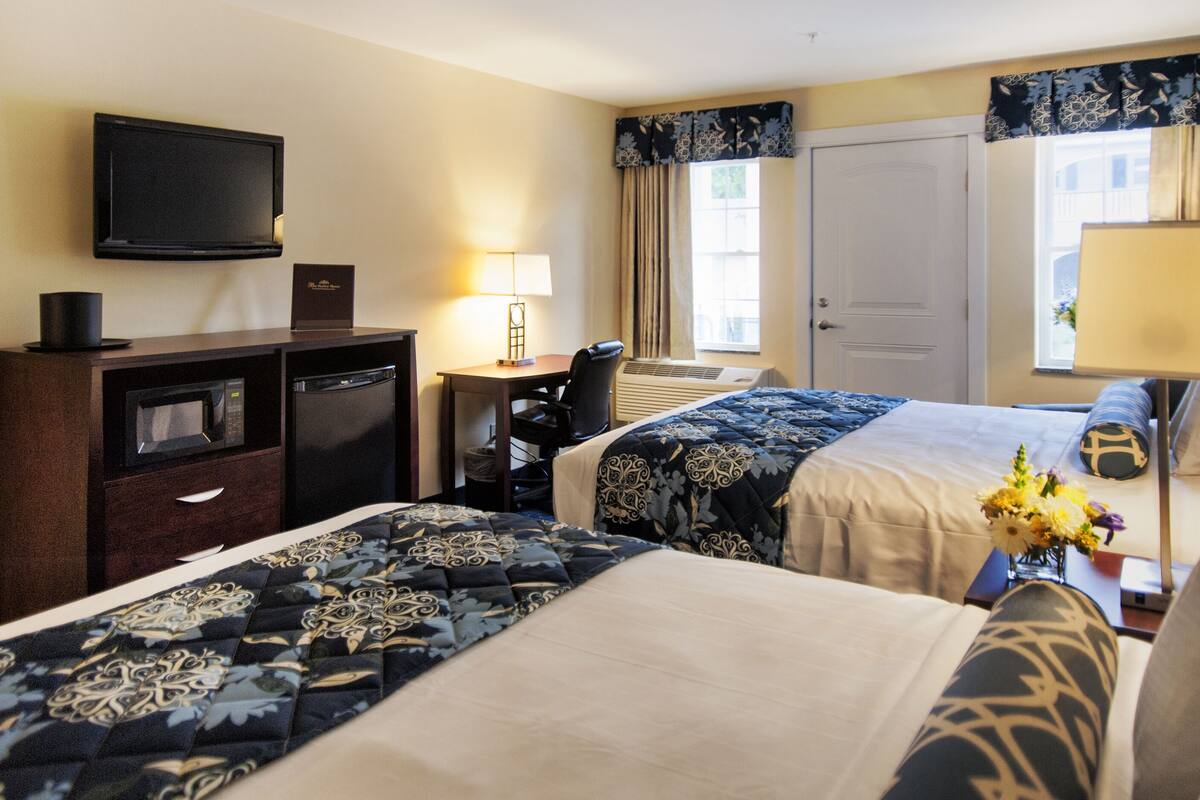 A hotel room with a bed, a desk with a chair, a television, a desk lamp, and a window with curtains.