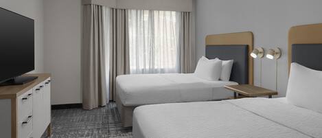 A hotel room with two beds, a television on a wooden stand, a desk with a lamp, and a patterned carpet.