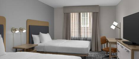 A hotel room with two beds, a desk, a chair, a television, and a window with curtains.