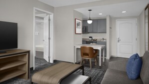 A hotel room with a TV, a bed, a sofa, a chair, a desk, a kitchenette, and a bathroom.