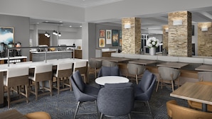 A modern hotel lobby with a bar, seating area, and a kitchen in the background.