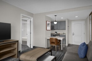 A compact hotel room with a bed, a television, a desk, and a kitchenette.