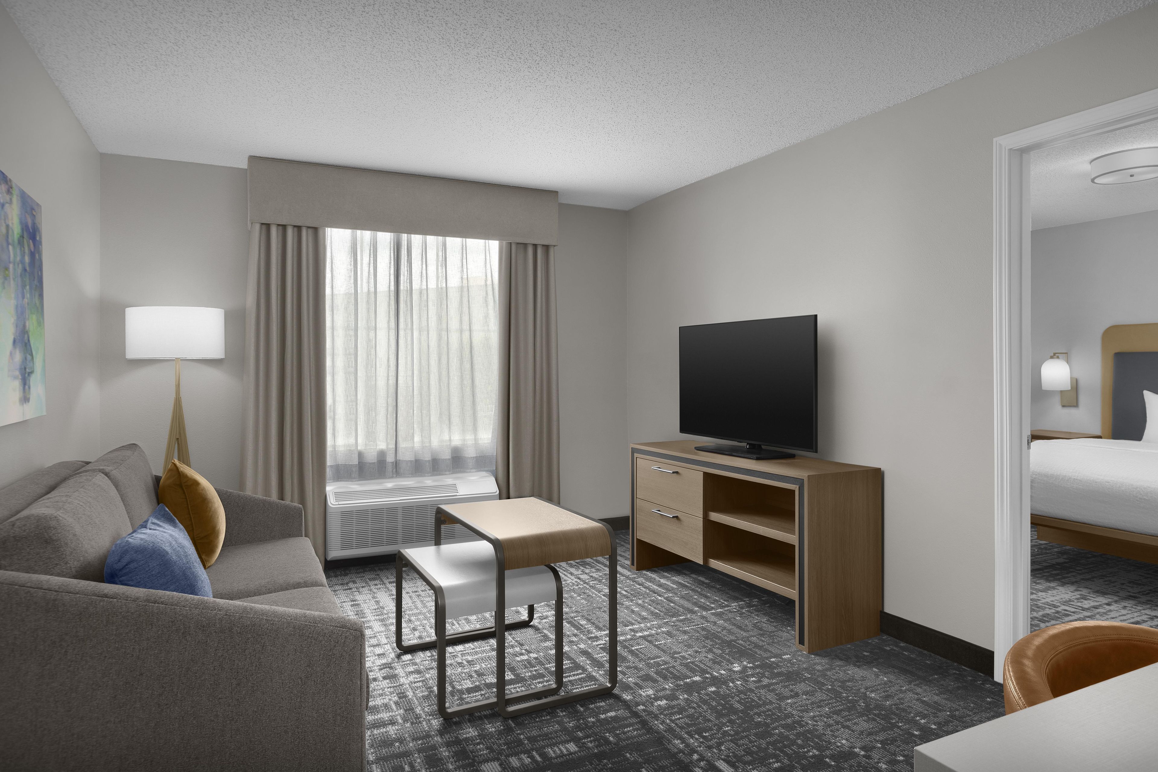 A hotel room with a sofa, a desk with a chair, a television, and a bed.