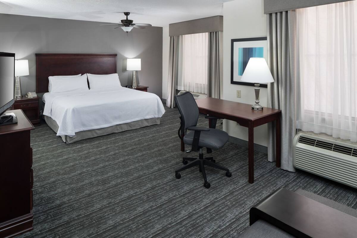 A hotel room with a bed, desk, chair, and a ceiling fan.