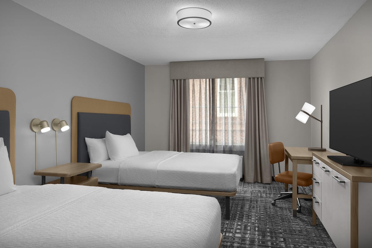 A hotel room with two beds, a desk, a chair, a television, and a window with curtains.