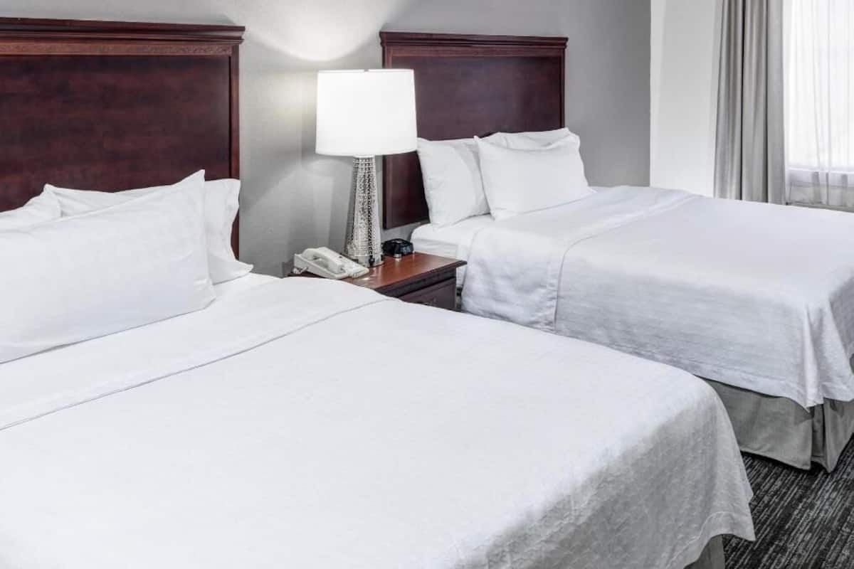 A hotel room with two beds, a nightstand with a lamp, and a telephone.