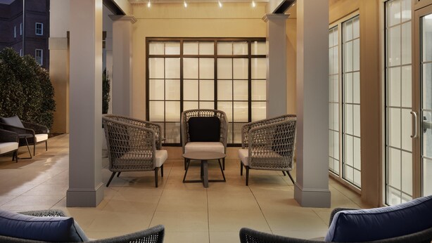 An outdoor seating area with wicker chairs and a table, a large window with a grid pattern, and a covered section with string lights.