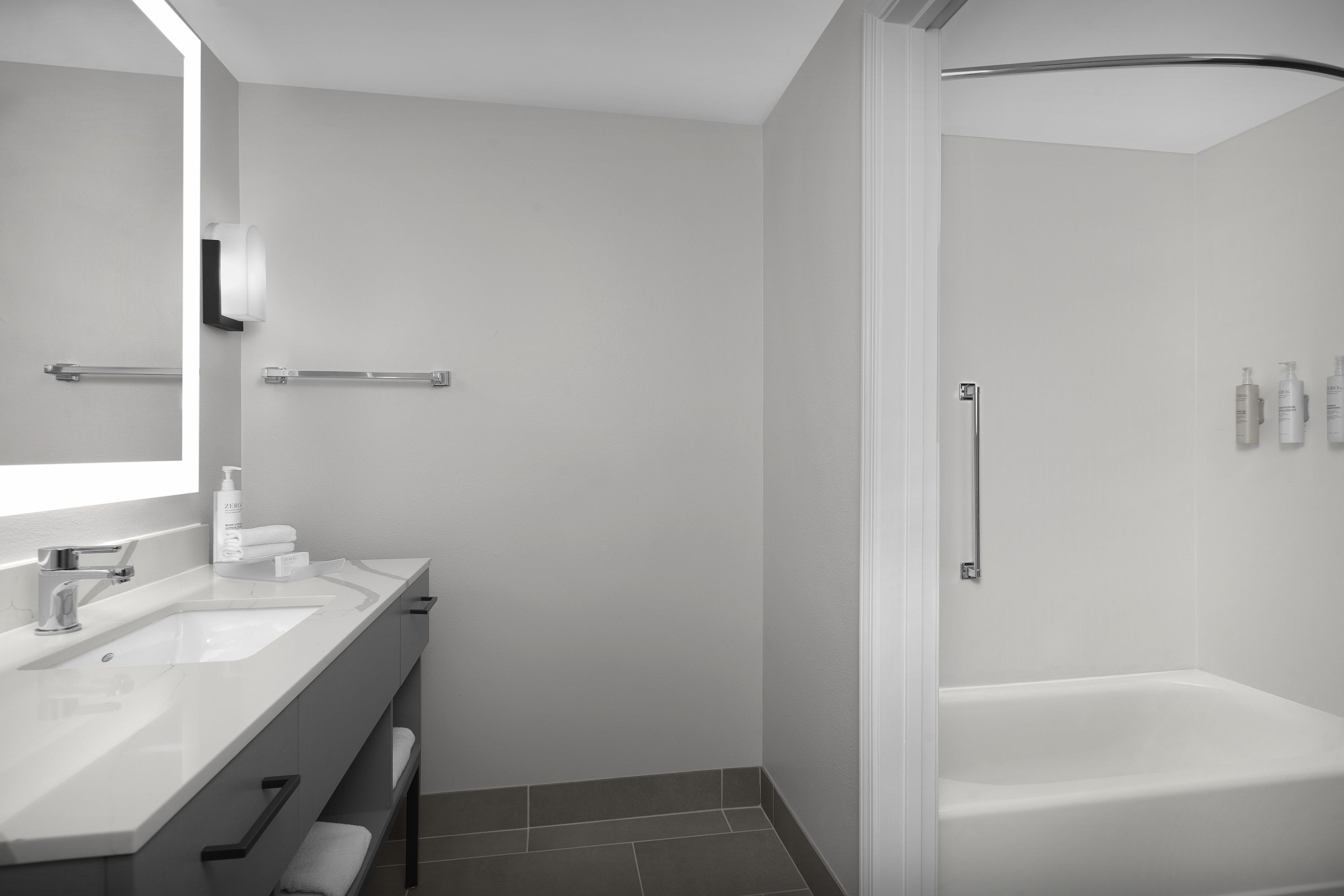 A modern bathroom with a white vanity, a large mirror, a bathtub, and a shower area.