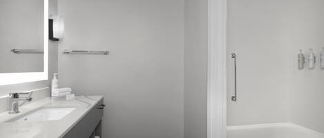 A modern bathroom with a white vanity, a large mirror, a bathtub, and a shower area.