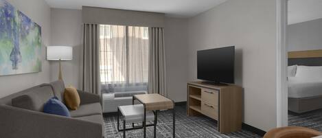 A hotel room with a sofa, a small table, a TV, a bed, and a window with curtains.