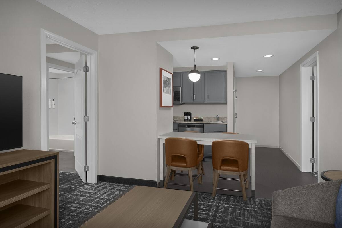 A modern hotel room with a dining area, kitchenette, and a TV.