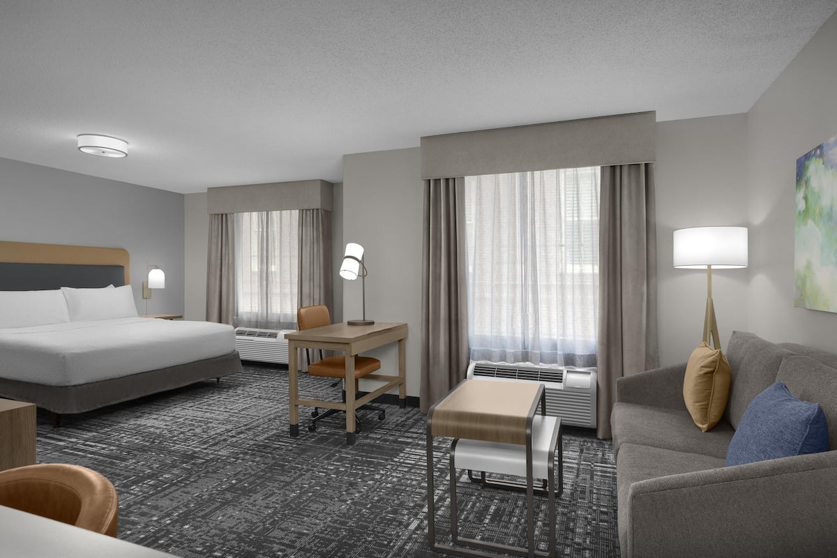 A hotel room with a bed, desk, chair, sofa, and a painting on the wall.
