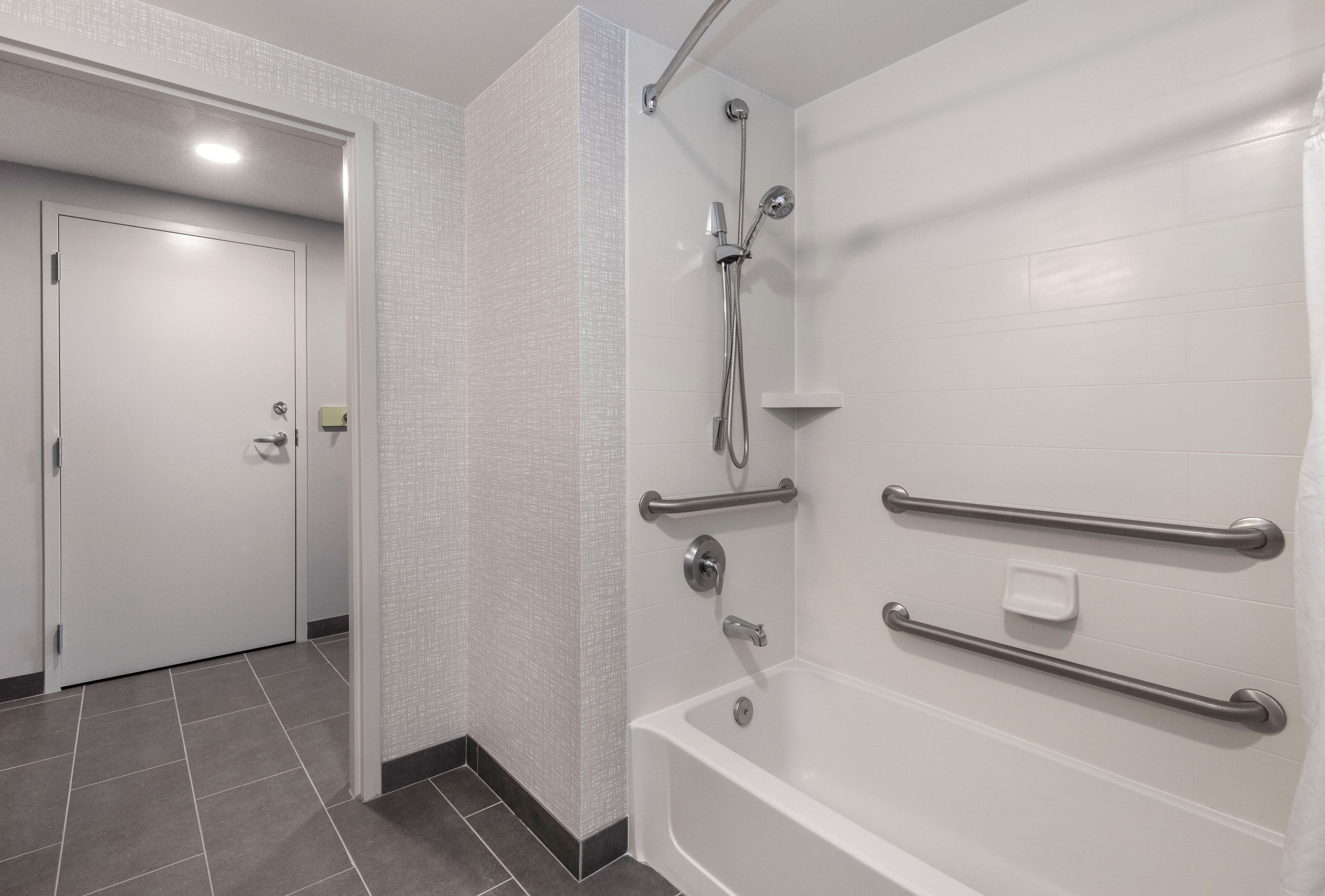 A bathroom with a white bathtub, grab bars, and a showerhead.