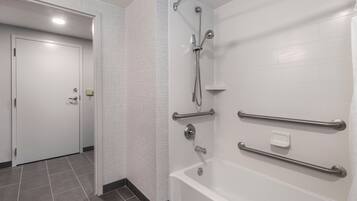 A bathroom with a white bathtub, grab bars, and a showerhead.