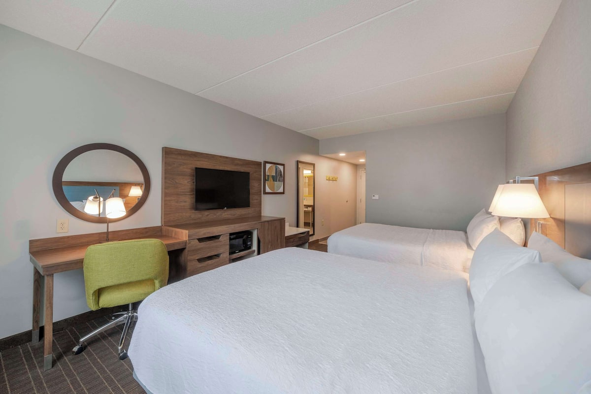A hotel room with two beds, a desk with a chair, a TV, and a mirror.