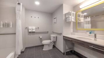 Un baño moderno con inodoro, lavabo y ducha. Hay barras de apoyo, un espejo y un perchero para toallas.