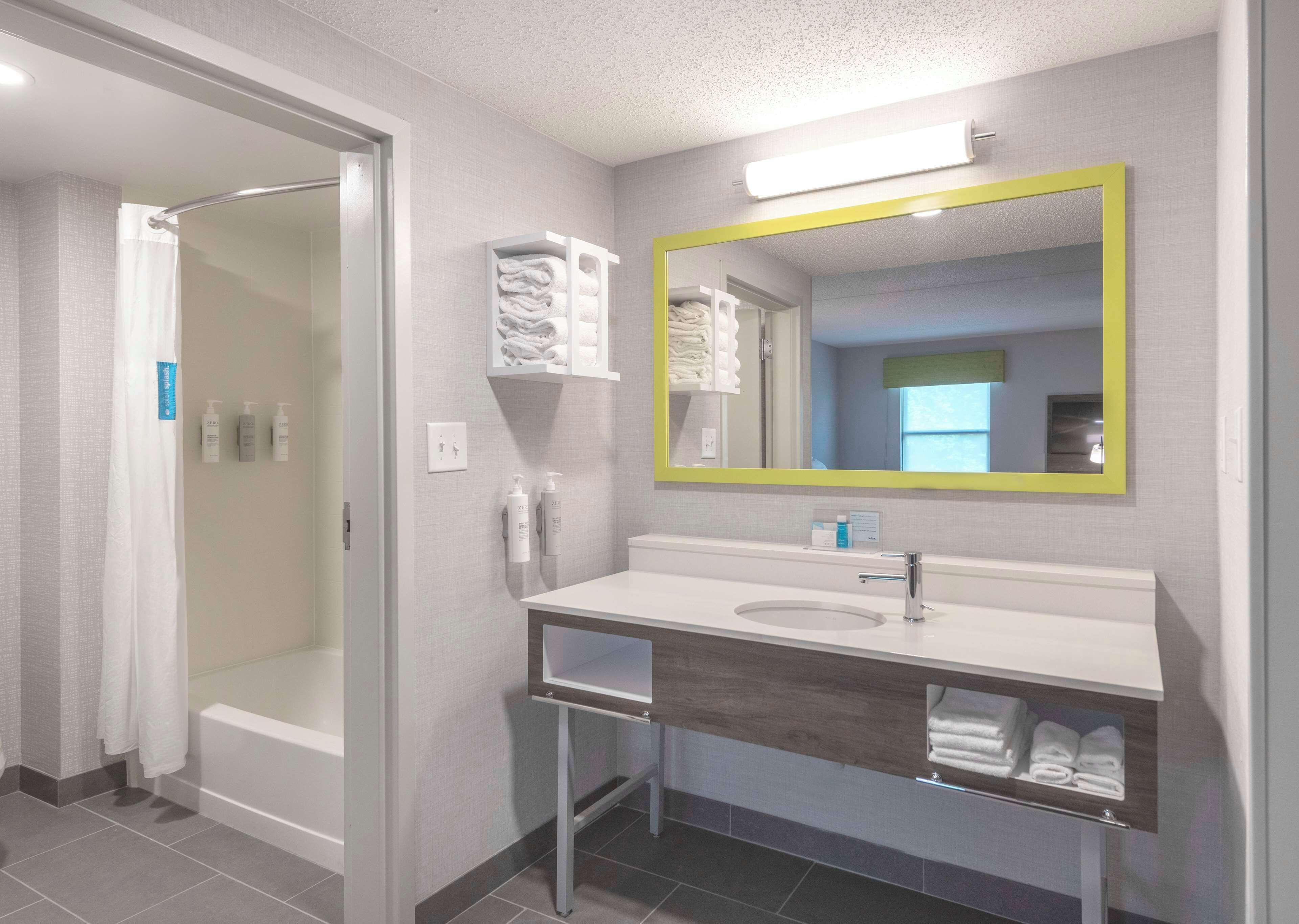 A modern bathroom with a walk-in shower, a sink with a mirror, and neatly folded towels on the wall.