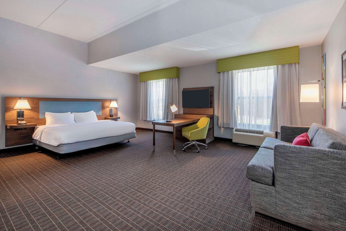 A hotel room with a bed, desk, chair, and sofa.