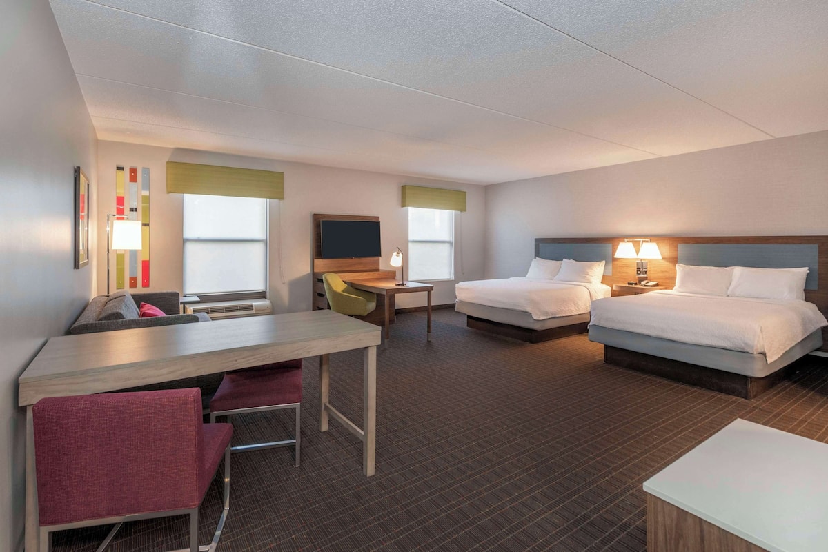 A hotel room with two beds, a desk, a chair, a TV, and a window with a view.