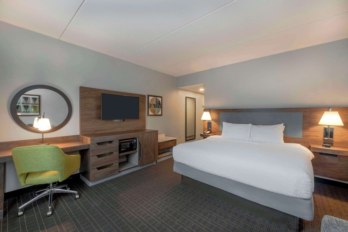 A hotel room with a bed, a desk with a chair, a television, and a mirror.