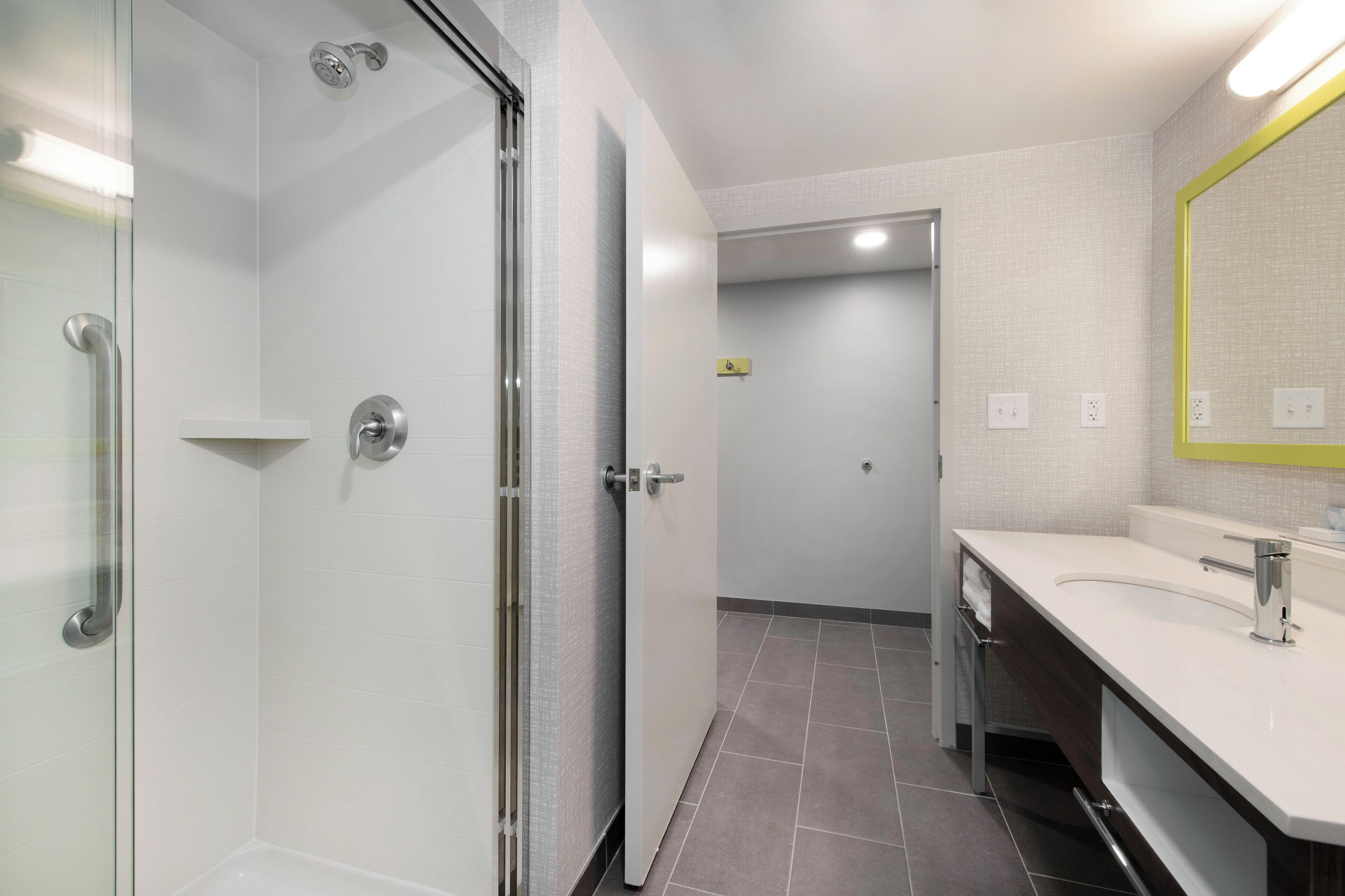 Un baño moderno con cabina de ducha de vidrio, un lavabo blanco con espejo y suelo de baldosas.
