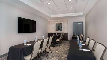 A conference room with a long table, chairs, a flat-screen TV, and water bottles on the table.