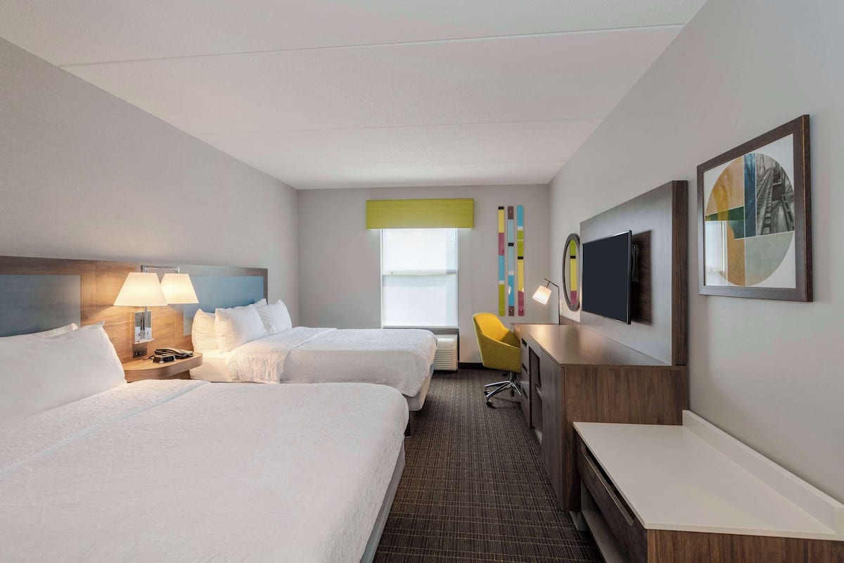 A hotel room with two beds, a desk, a chair, a TV, and a window.