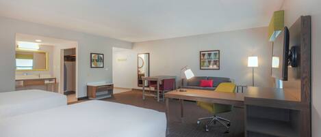 Habitación de hotel con dos camas, un escritorio, una silla, un sofá, un televisor y un espejo.