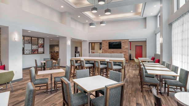 A modern hotel lobby with multiple seating areas, a reception desk, and a TV screen.