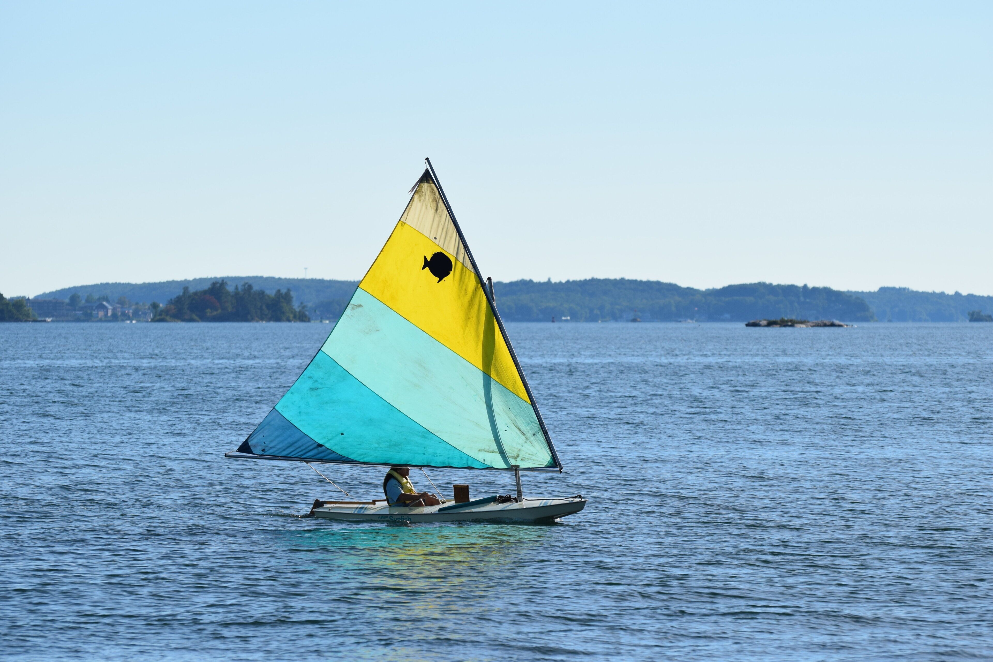 A sailboat with a colorful sail on a calm body of water.