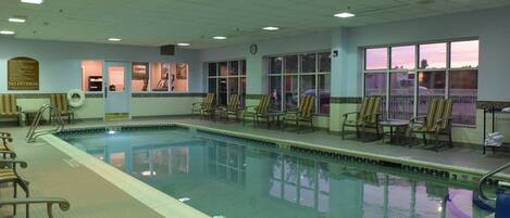 An indoor swimming pool with lounge chairs and a clock on the wall.