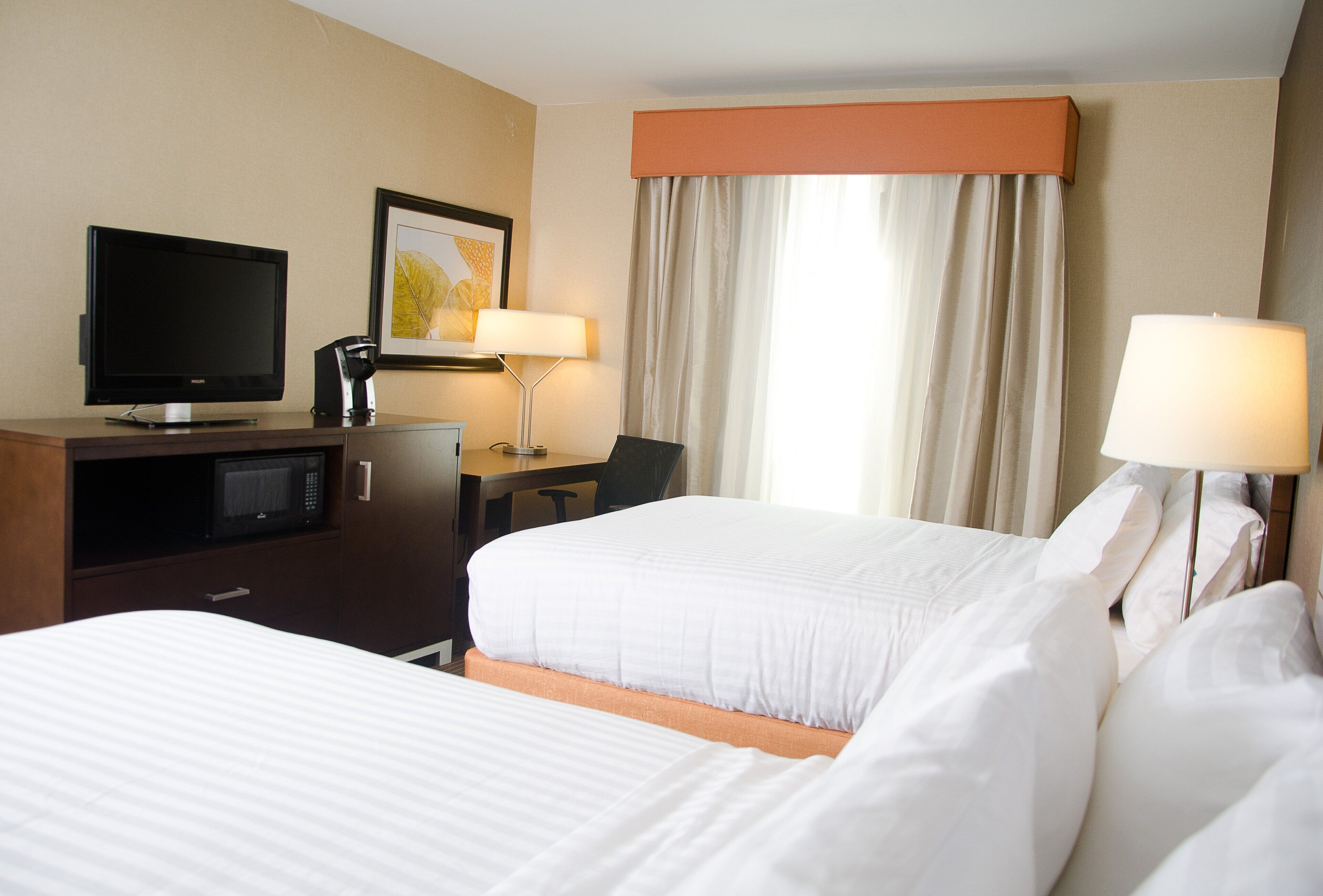 Hotelkamer met twee bedden, een bureau met een computer, een televisie, een magnetron en twee lampen.